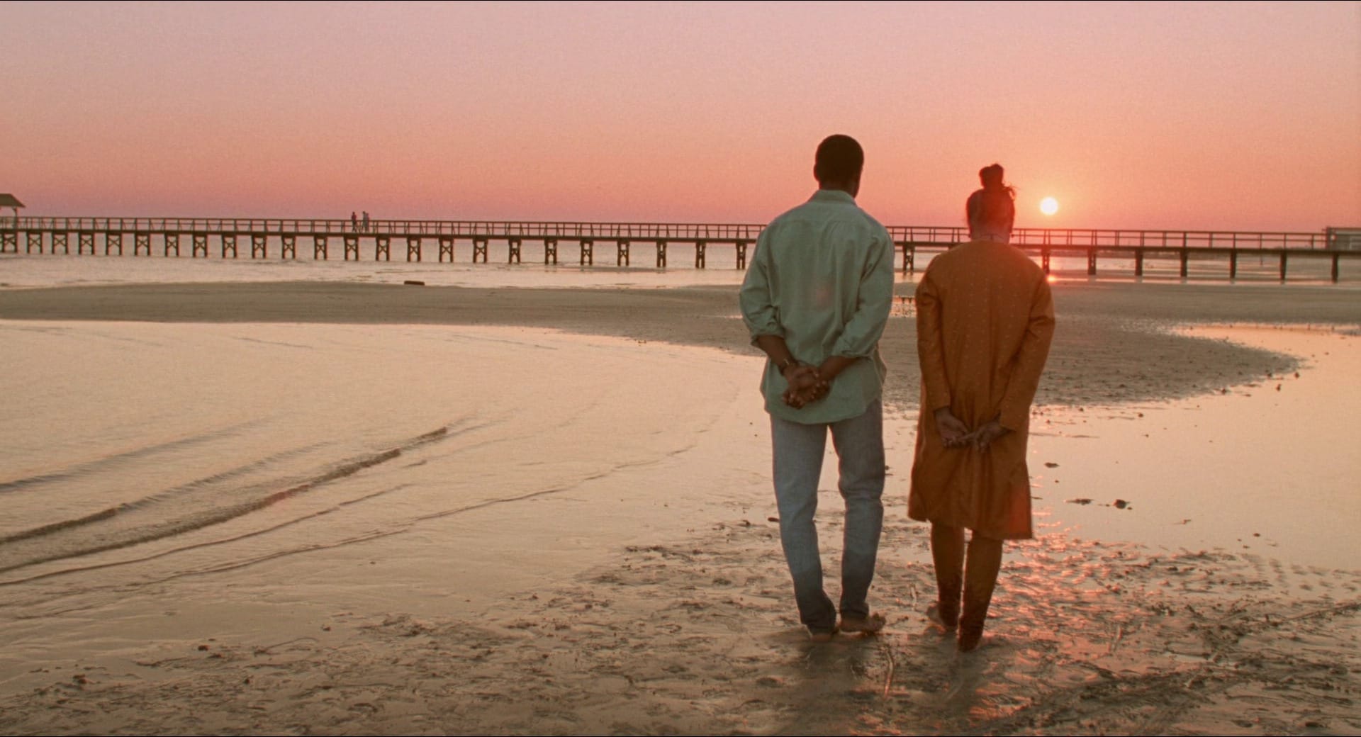 Seen from behind, Denzel Washington and Sarita Choudhury walk on a beach in Mississippi Masala