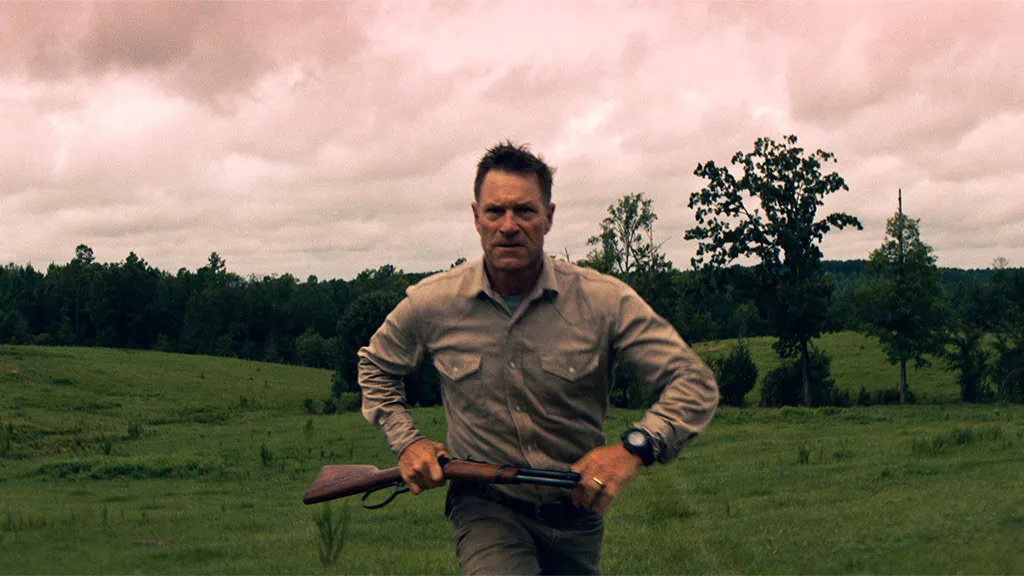 Aaron Eckhart runs through a field while holding a rifle in Thieves Highway