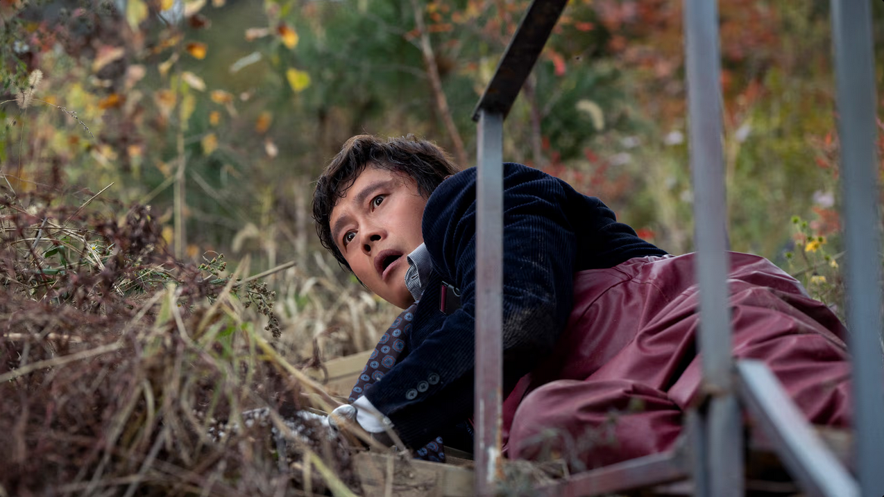 Lee Byung-hun has fallen to the ground and looks comically shocked in No Other Choice