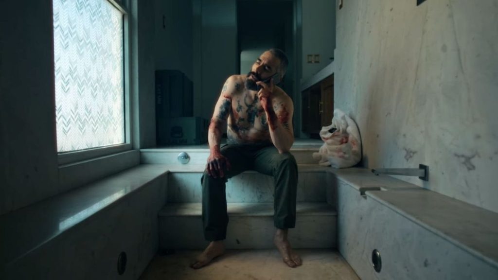 A bloody Omar Chaparro takes a phone call while sitting on the steps of an empty bathtub in Vengeance