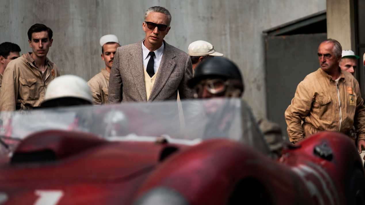 Adam Driver as Enzo Ferrari looking at a red car in Ferrari