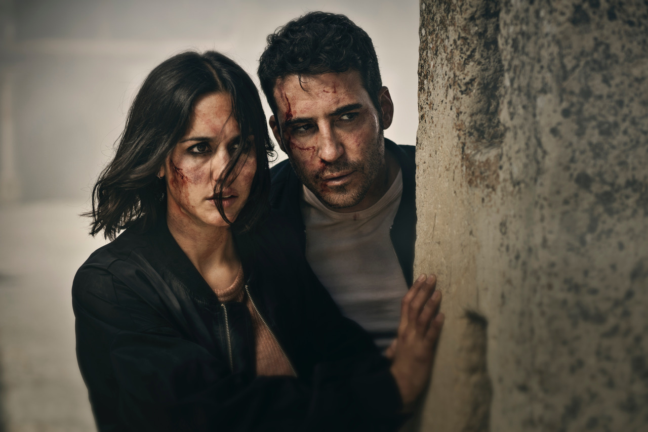 In 30 Coins, Megan Montaner and Miguel Ángel Silvestre peer out from behind a wall with blood on their faces