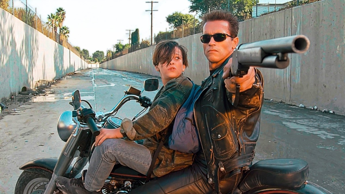 In T2, the Terminator points a shotgun towards the camera while young John Connor looks on as they sit on a motorbike in the LA River