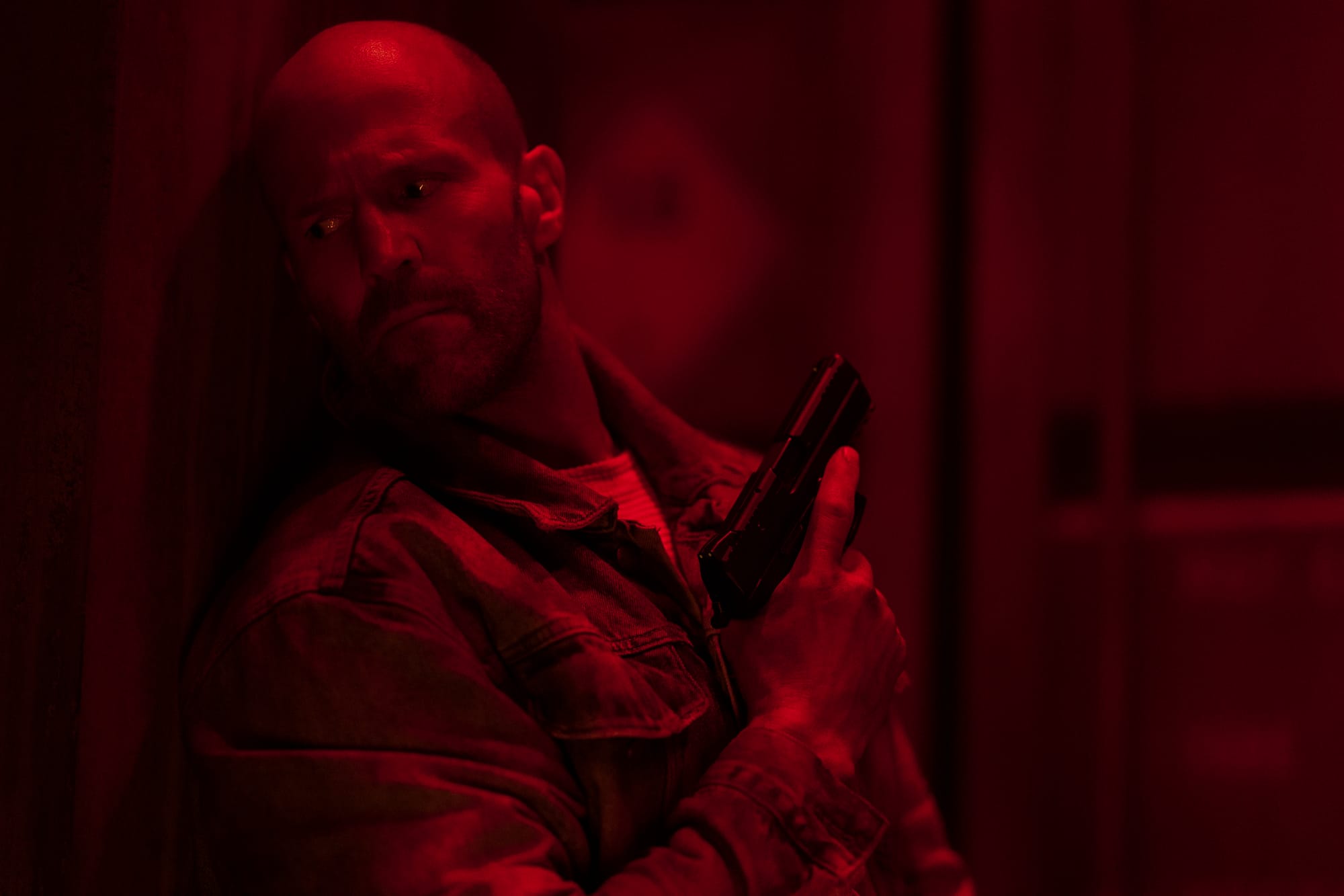 A red-tinted Jason Statham holding a pistol on a boat in a red-tinted image from Mutiny