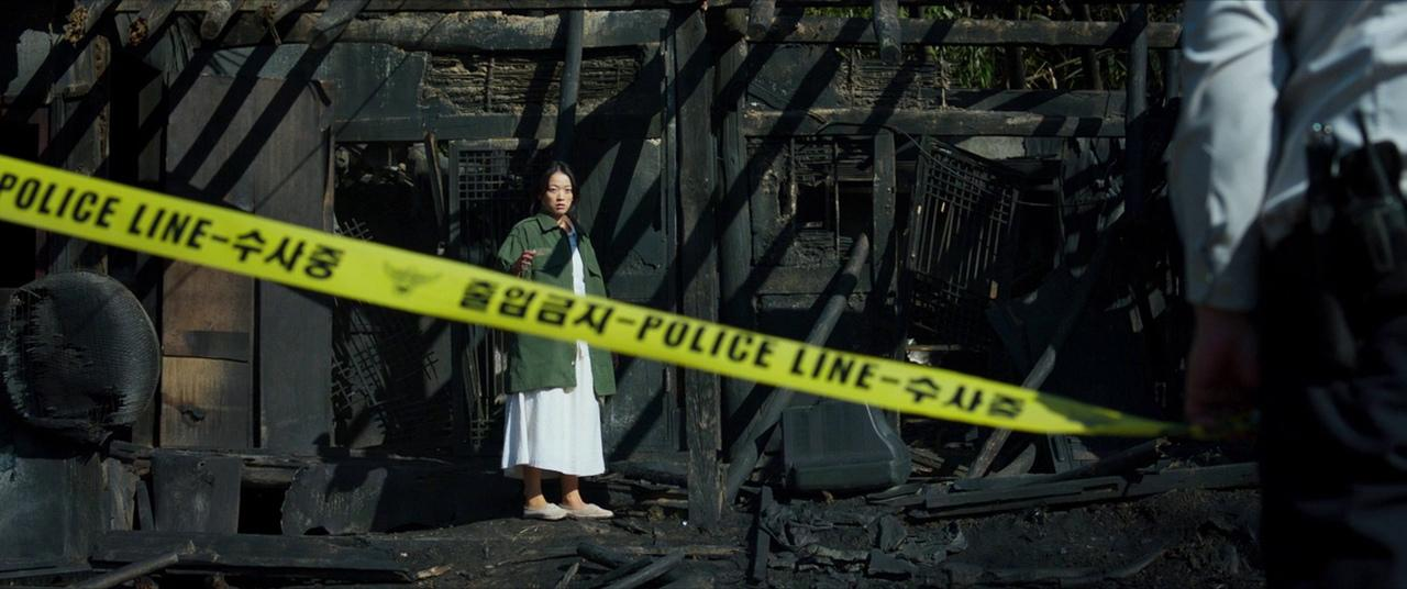 A woman stands behind police caution tape in The Wailing