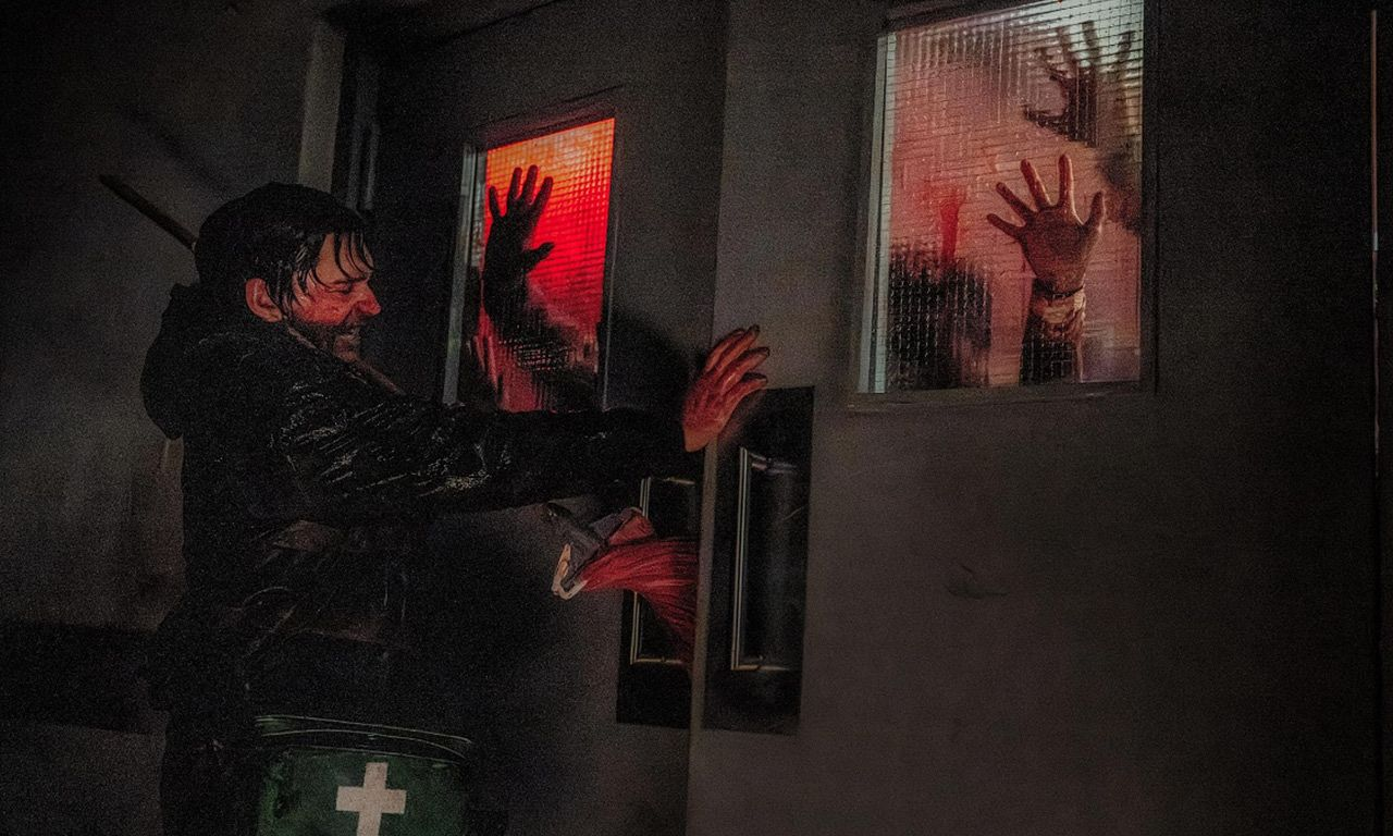 Austin Abrams bars a door shut from a lot of zombies on the other side in Resident Evil