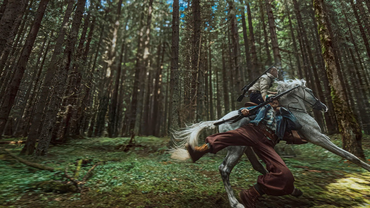 A man is grabbed by another man riding fast on a horse in a forest in Hope