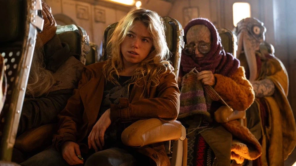 Milly Alcock as Supergirl, sitting on a crowded bus with alien passengers