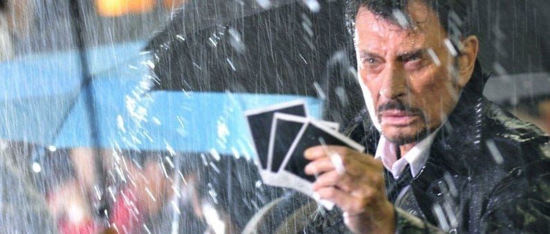 Johnny Hallyday holds up three polaroid photos in the rain in Vengeance
