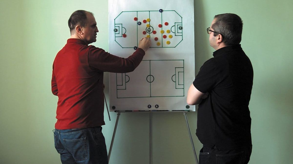 In Infinite Football, director Corneliu Porumboiu and subject Laurentiu Ginghina stand in front of a paper board of a soccer field, as Ginghina places tokens representing players on it