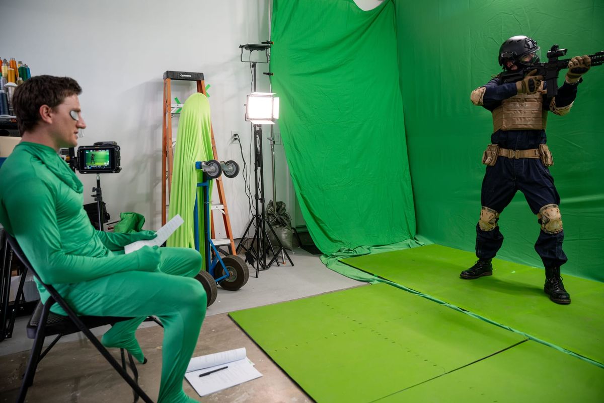 Jason Trost directs while wearing a green suit, instructing an actor dressed as a soldier in front of a green screen