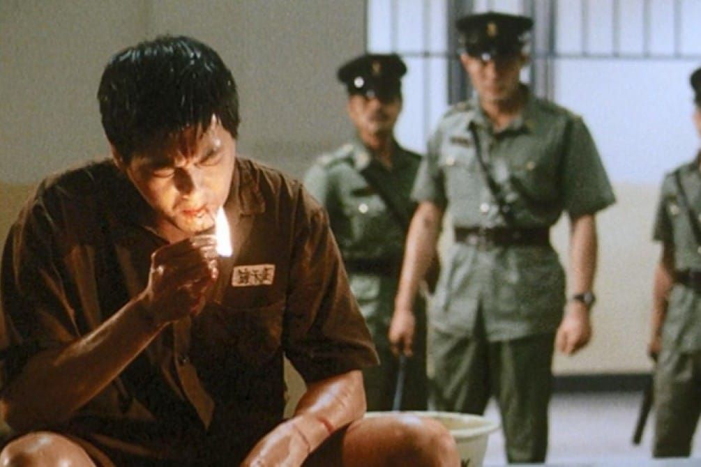 Chow Yun-fat smokes a cigarette in a Prison on Fire movie as guards look on menacingly