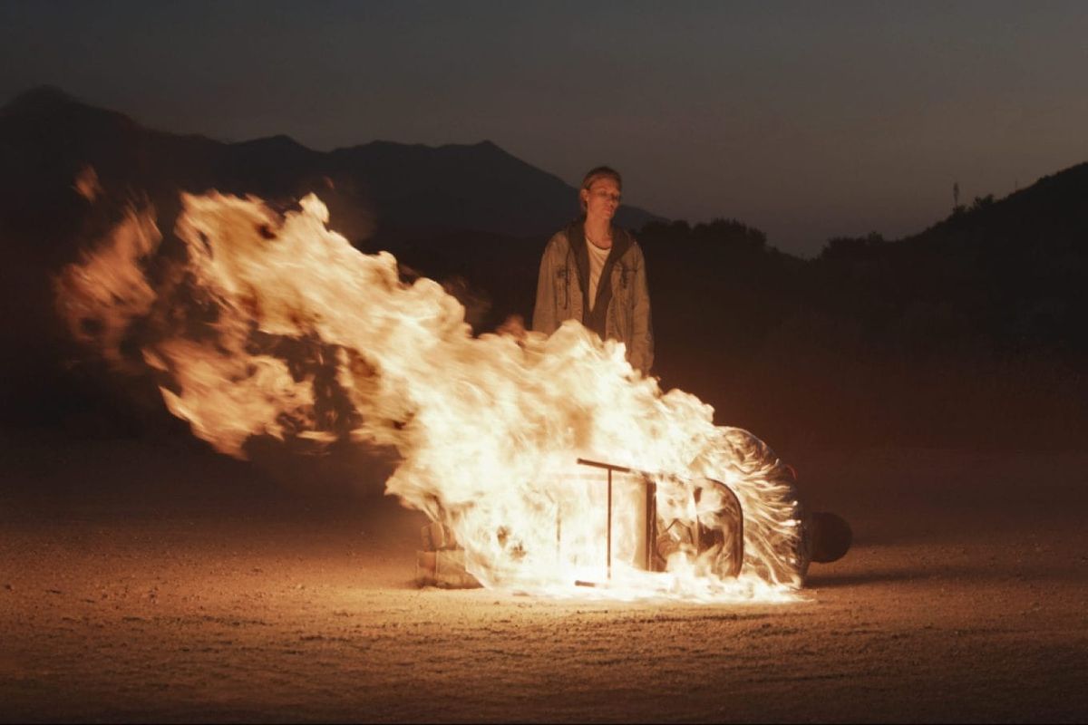 Michaela McManus stands in front of a man who is burning while tied to a chair, fallen to the ground in Redux Redux