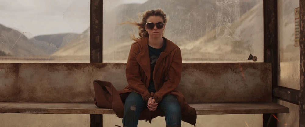 Milly Alcock as Supergirl, setting on a bus bench in the middle of a desert