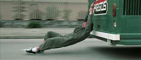 Jackie Chan holds onto the back of a bus while skidding on the street in Police Story