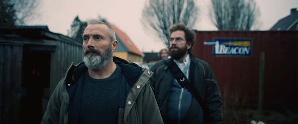 A determinted Mads Mikkelsen and Nikolaj Lie Kaas walk past a fence in Riders of Justice