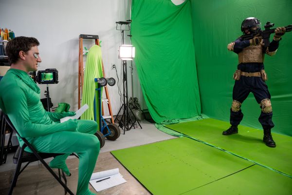 Jason Trost directs while wearing a green suit, instructing an actor dressed as a soldier in front of a green screen