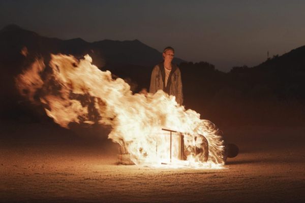 Michaela McManus stands in front of a man who is burning while tied to a chair, fallen to the ground in Redux Redux