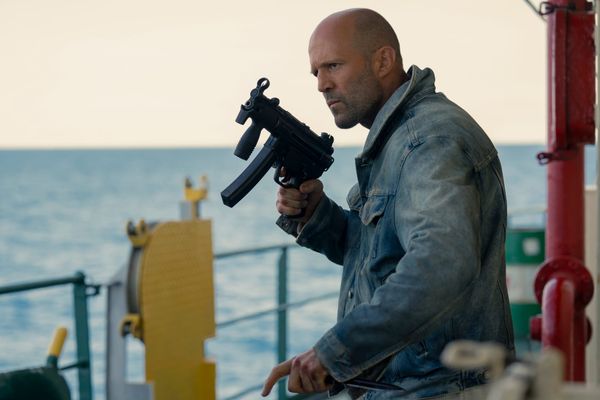 Jason Statham, wearing a denim jacket and holding a submachine gun on a boat in Mutiny