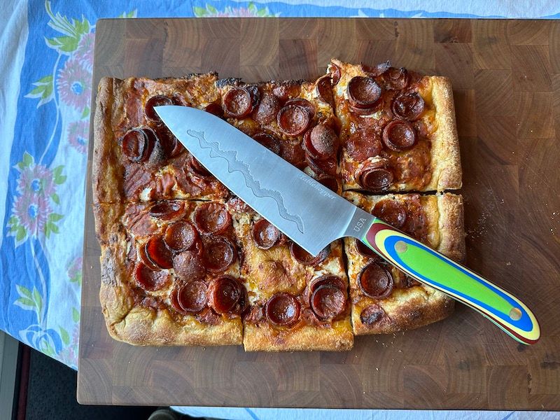 custom-engraved, Teton Edge santoku from New West KnifeWorks resting over pizza