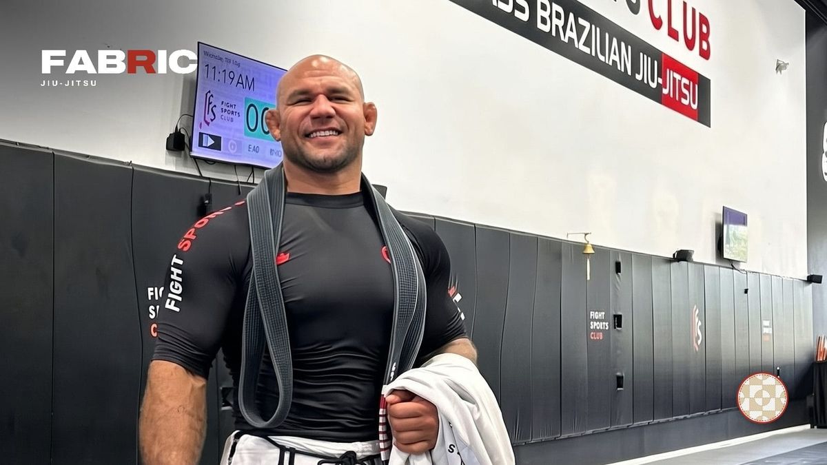 Roberto “Cyborg” Abreu smiling in a Fight Sports rash guard with his black belt over his shoulders, with the Fabric Jiu-Jitsu wordmark