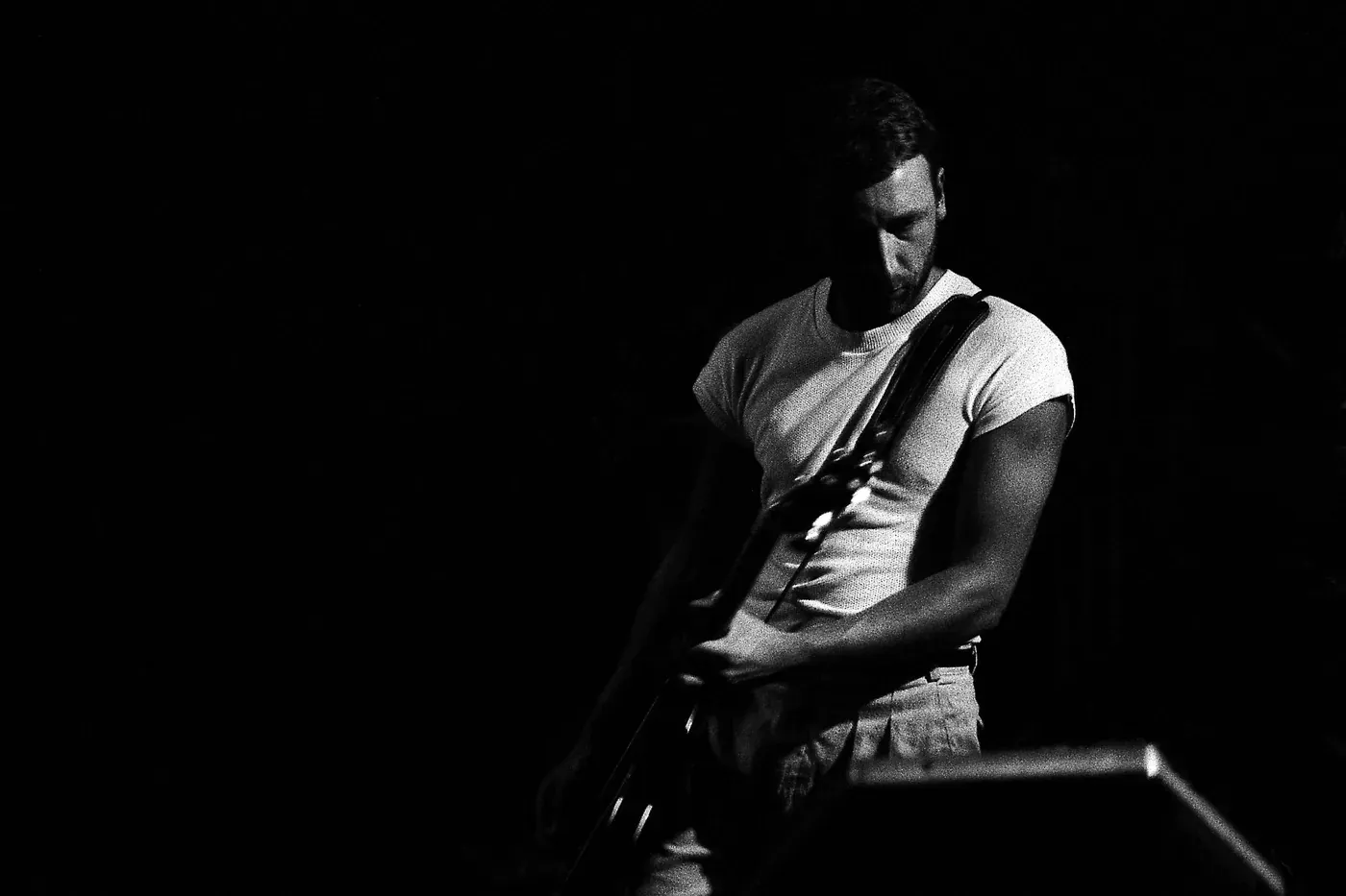 Black and white photo of a New Order member playing guitar on stage at the SFX in Dublin in 1983