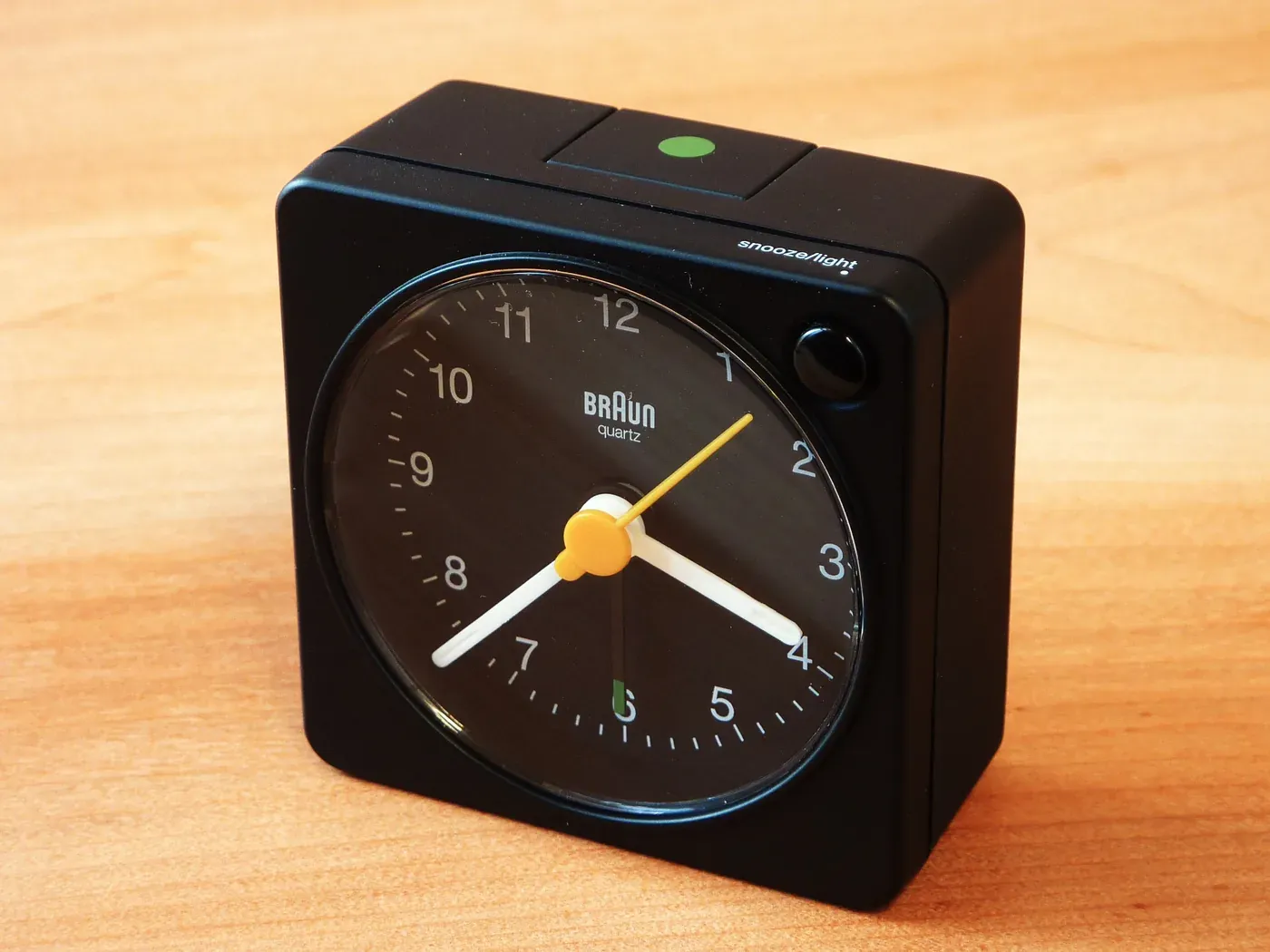 Black Braun BC02 travel alarm clock with a yellow second hand on a wooden surface