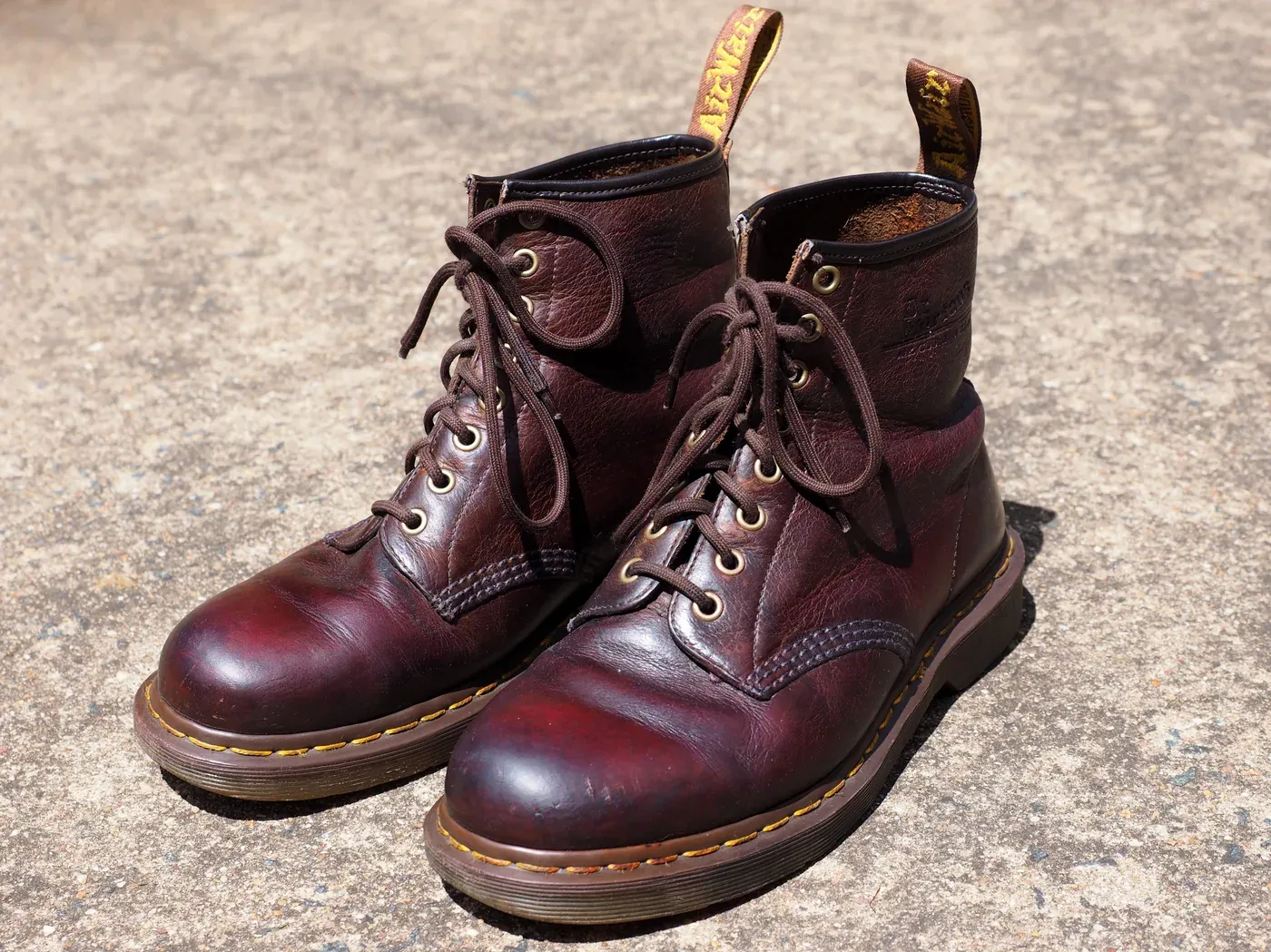 Pair of well-worn brown Dr. Martens 1460 leather boots with yellow welt stitching on pavement