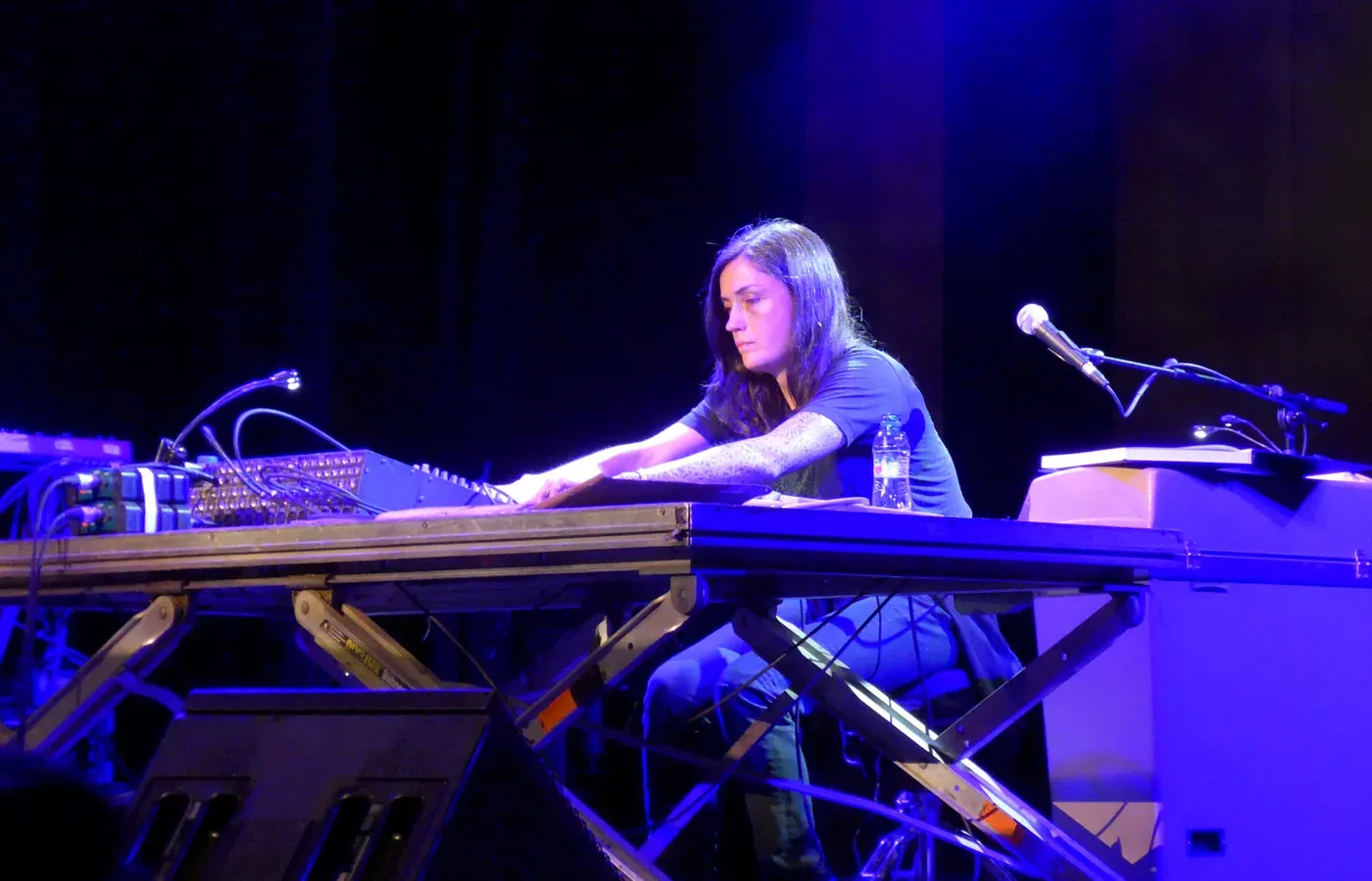 Liz Harris of Grouper seated at her equipment under blue stage light