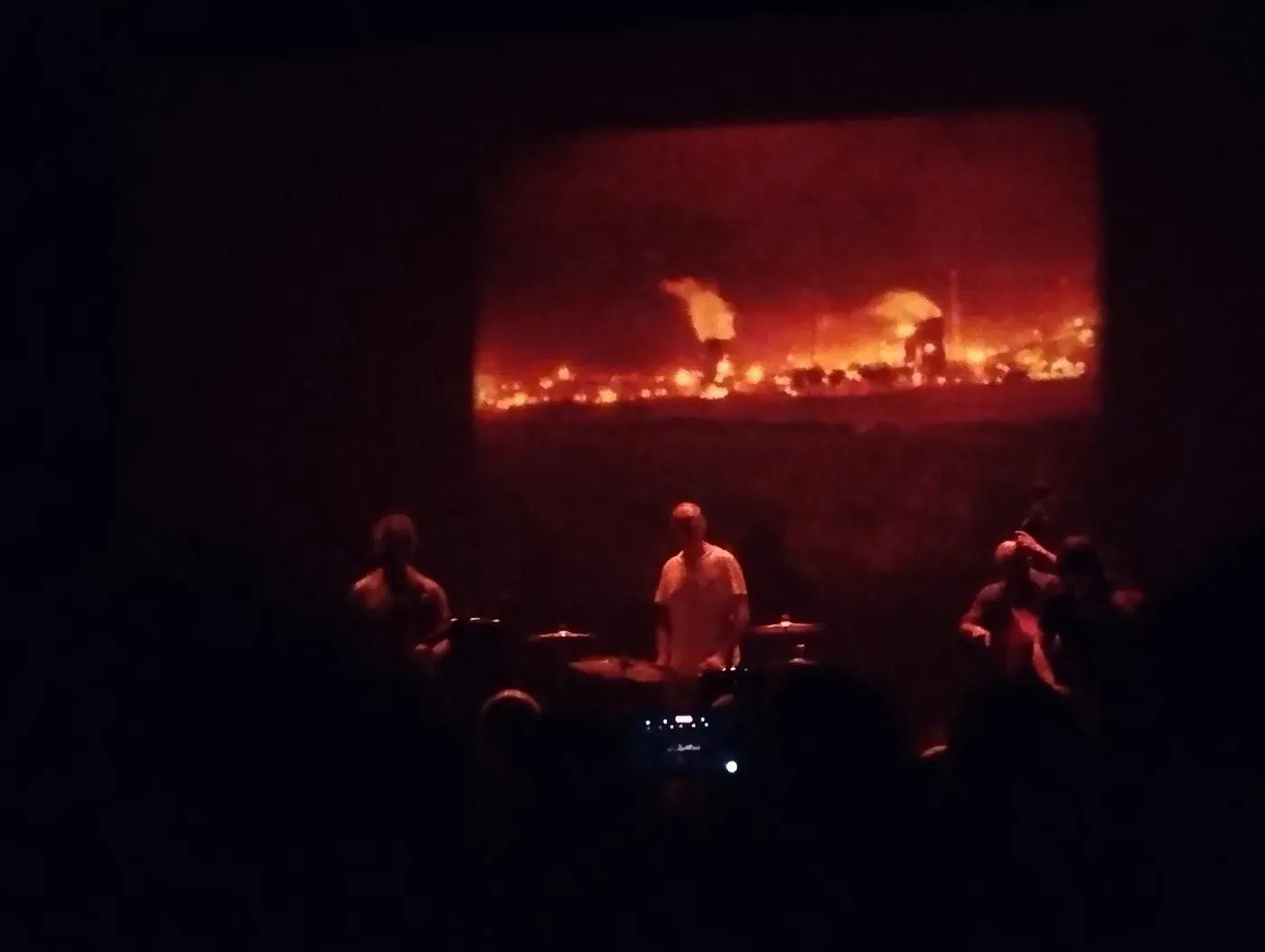 Godspeed You! Black Emperor performing in near darkness beneath a projection of flames