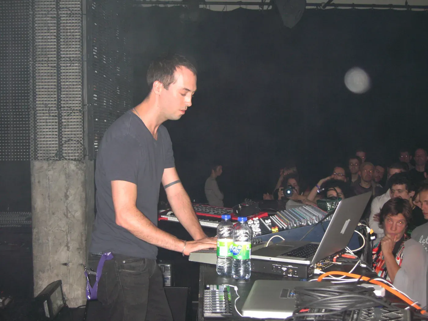 Tim Hecker performing at a mixing desk and laptop in a dim concrete venue