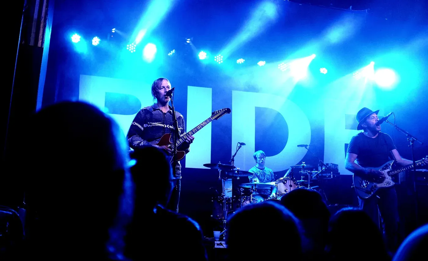 Ride performing in blue stage light with the band's name on the backdrop at Saint Andrew's Hall, Detroit