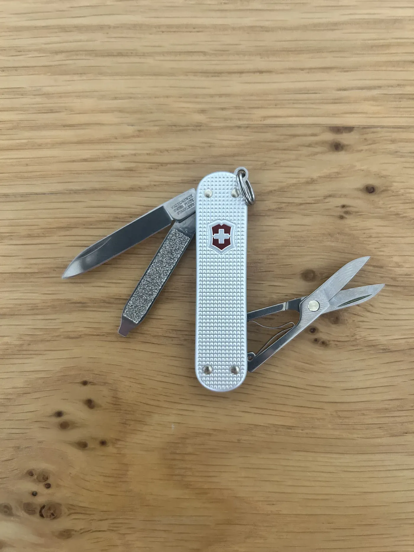 Silver Victorinox Classic SD Alox pocket knife with its blade and scissors opened on a wooden table