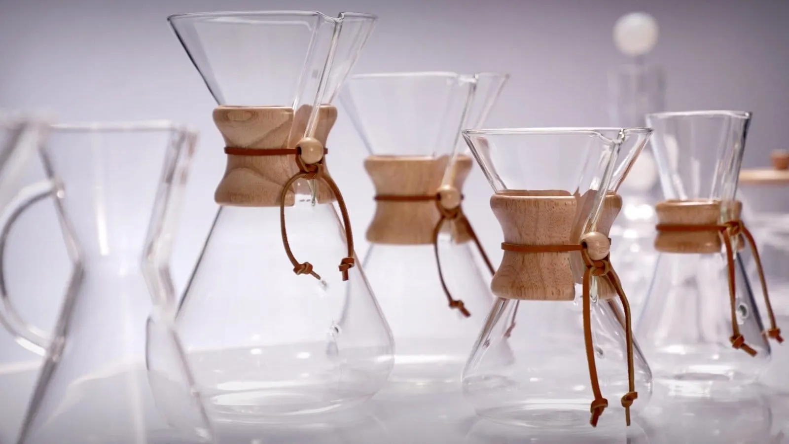 A row of Chemex Classic Series glass coffeemakers with wooden collars and leather ties on a white surface