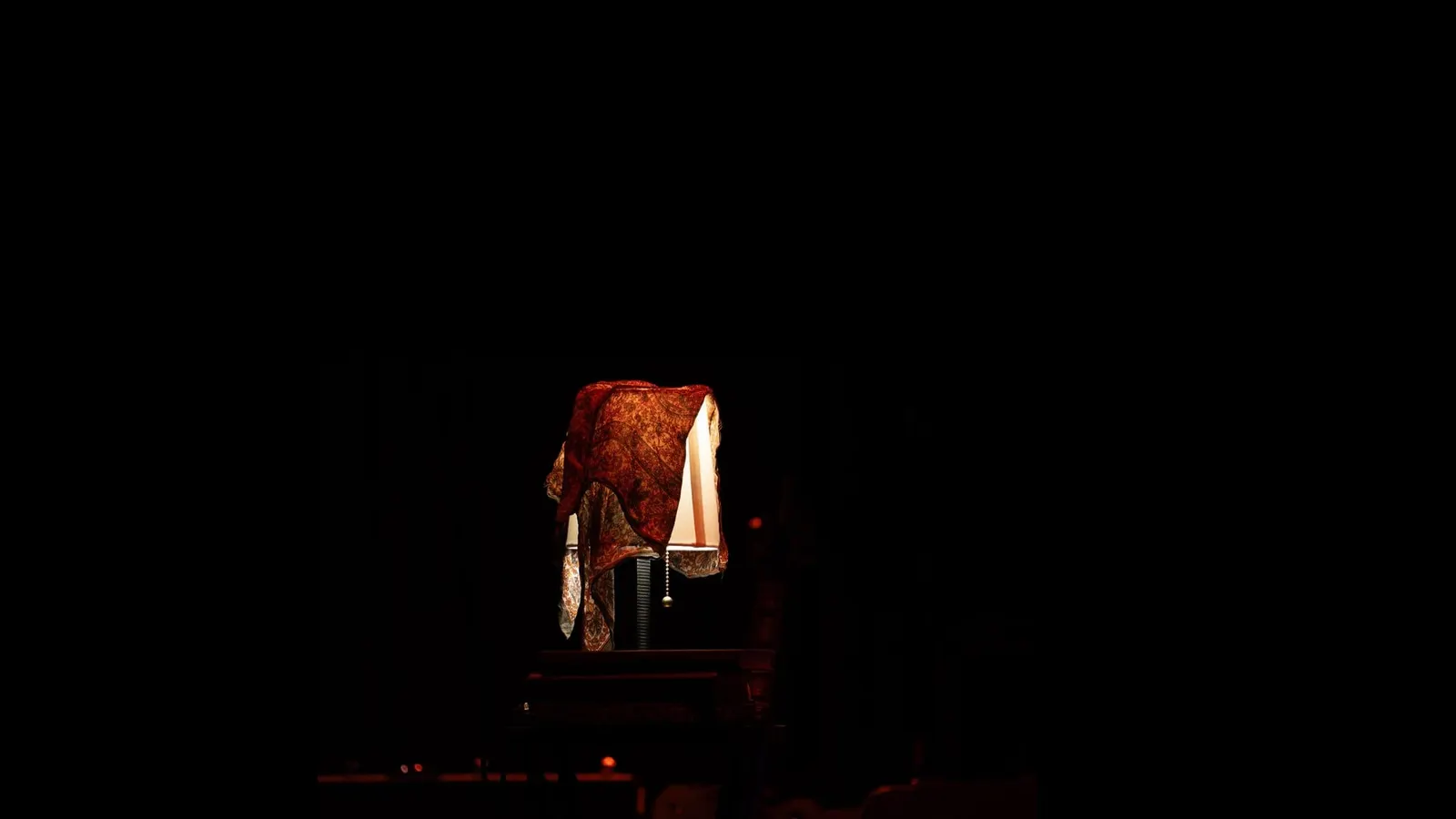 Single cover for It's Safe To Close Your Eyes: a lamp glowing under a draped, patterned rust colored cloth in an otherwise black room