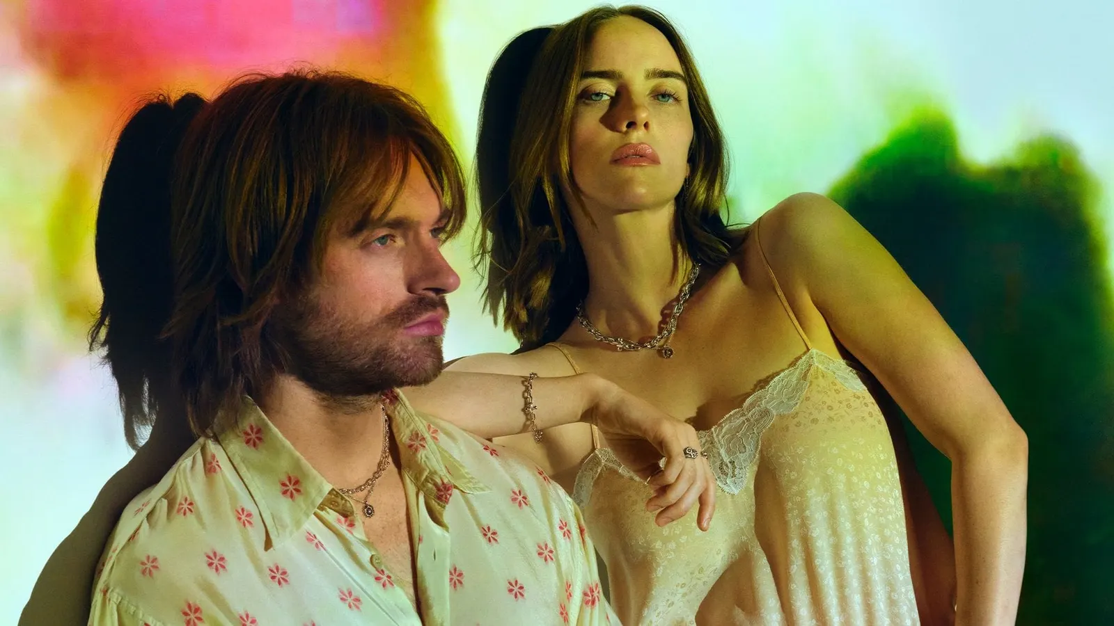 Billie Eilish and FINNEAS in the John Hardy campaign, wearing silver chain necklaces, a bracelet and rings against a blurred wash of green and pink light