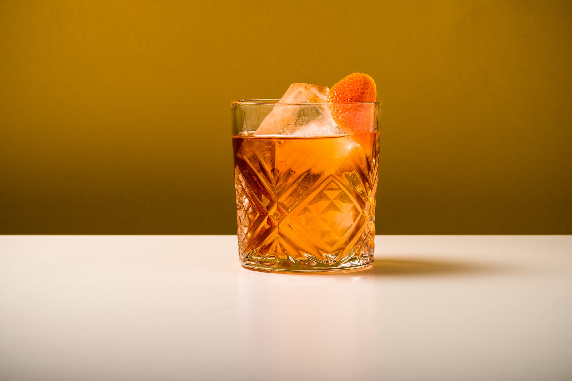 Orange cocktail in a cut crystal glass with ice and a citrus wheel garnish against a warm golden background