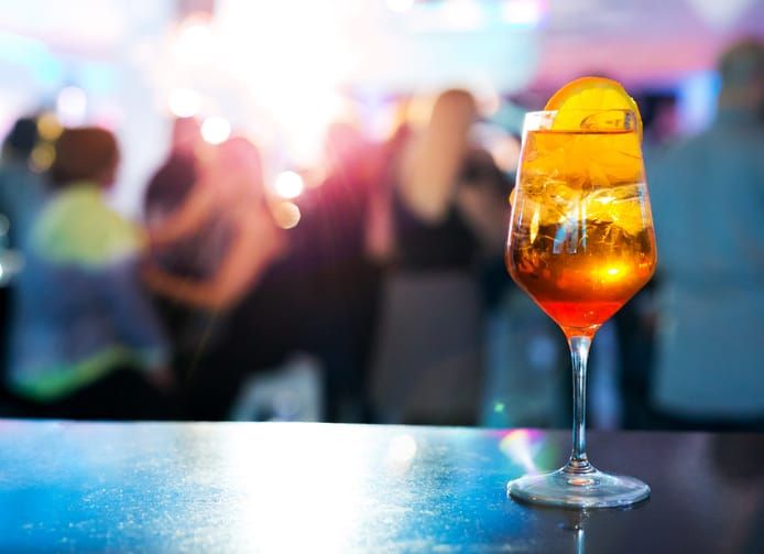 An Aperol Spritz on a bar with blurred party atmosphere in the background.