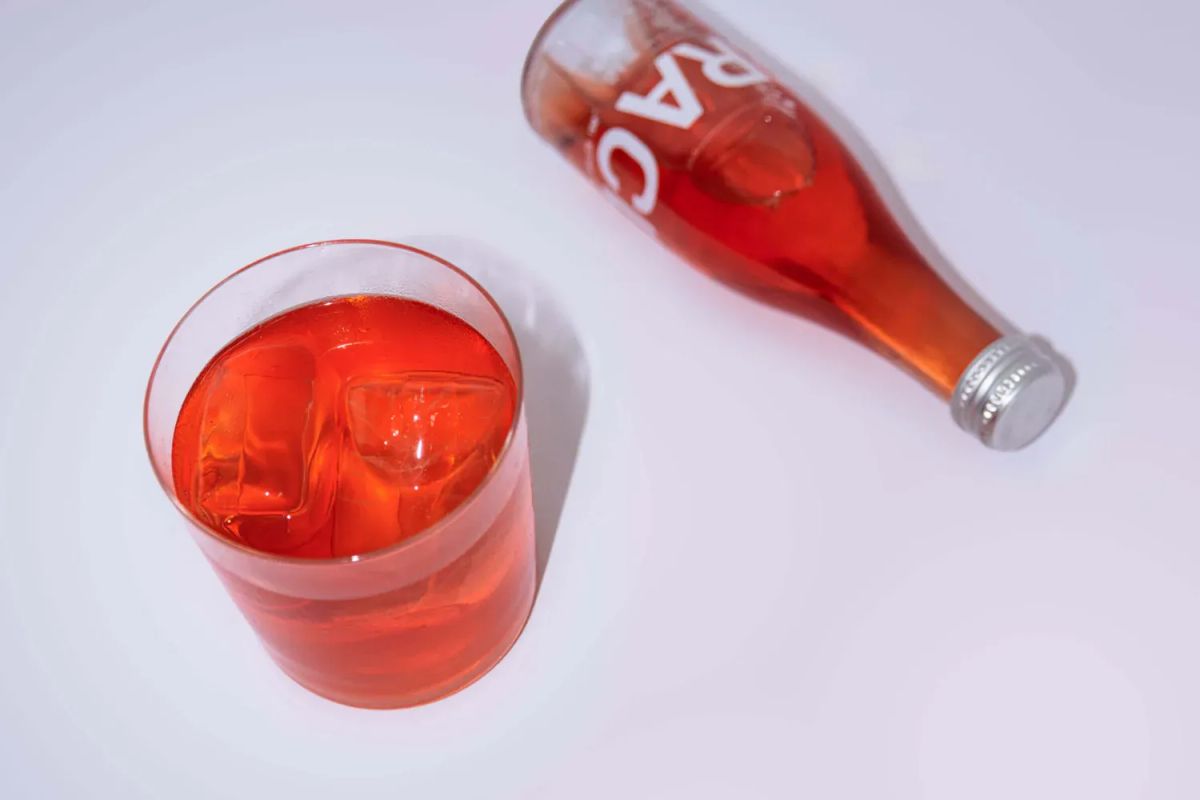 A bottle of Club Mera lying next to a glass of the same over ice, on a white background