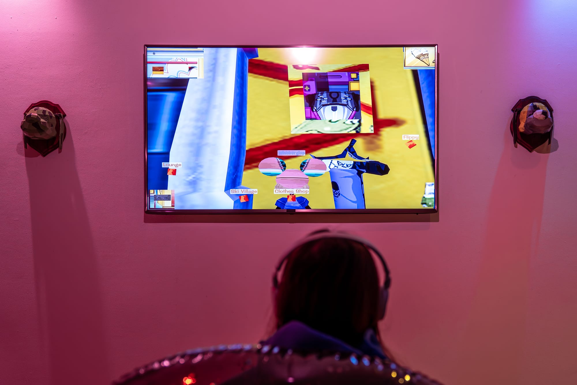 A player wearing headphones sits close to a screen showing TEXTURETOWN in a gallery installation