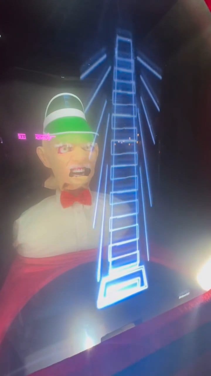 An animatronic carnival barker head beside a glowing vector-graphics tower