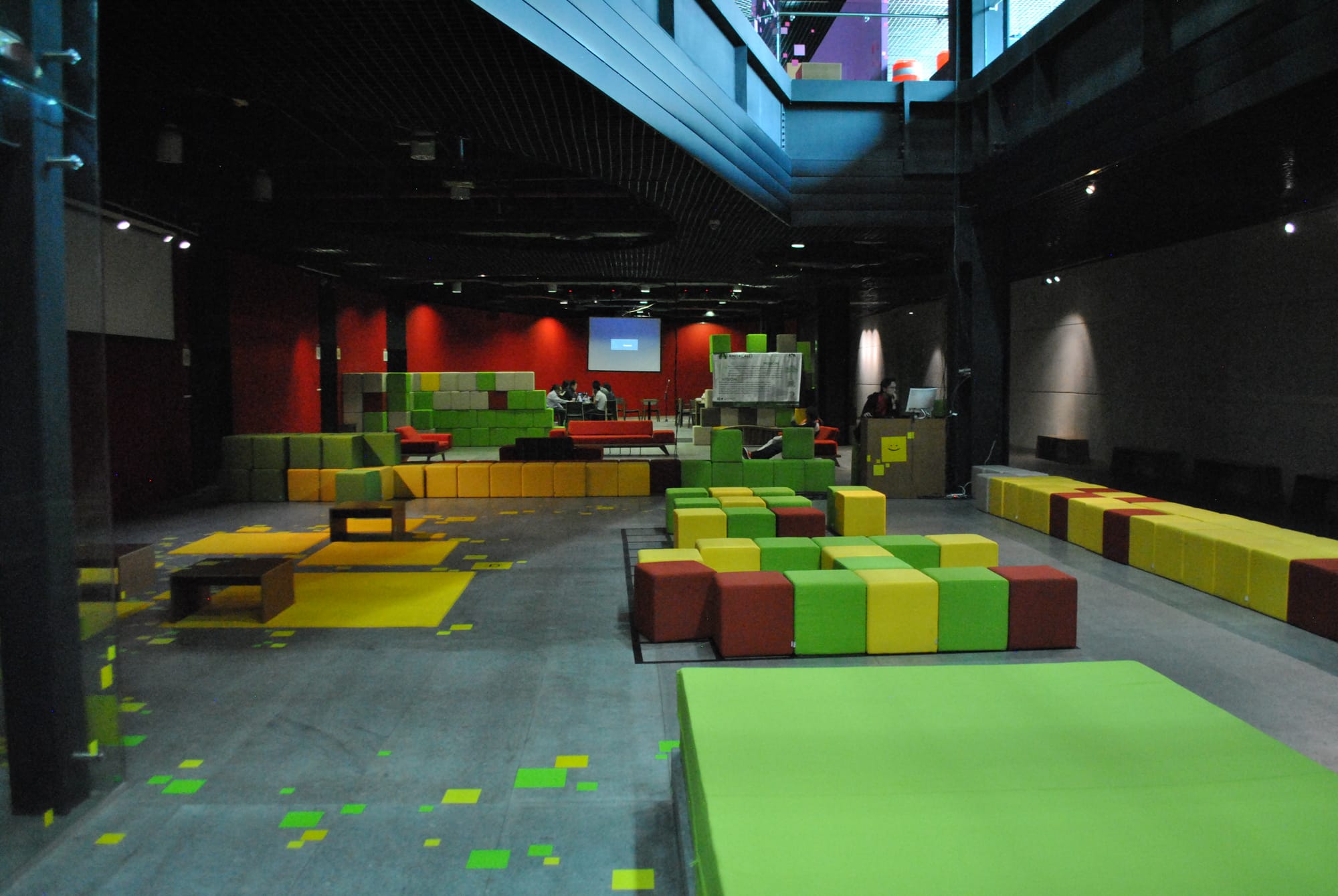 Visitors on the exhibition floor of the Centro de Cultura Digital, with low modular seating in green, yellow and orange