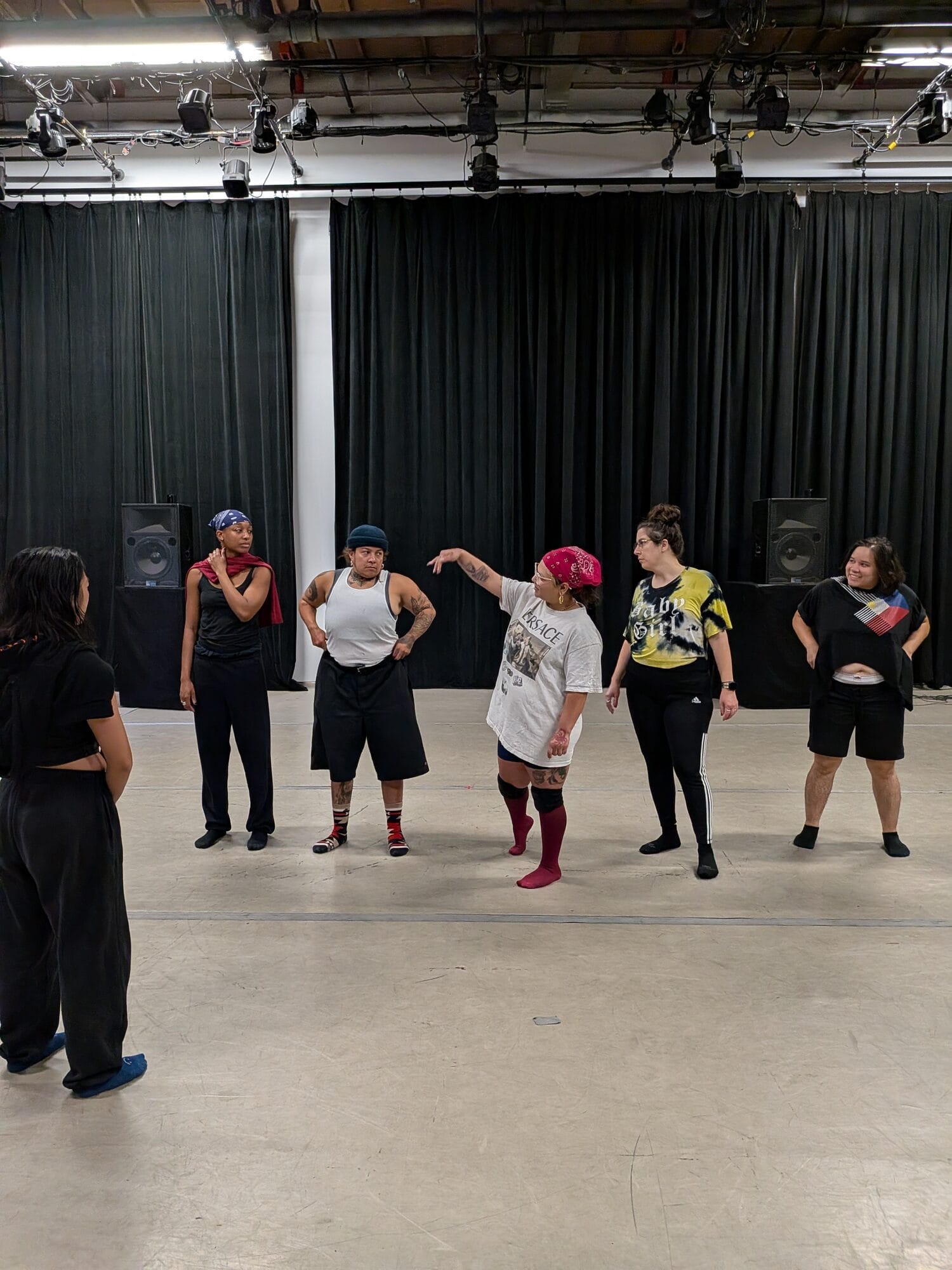 The company standing in a circle in a rehearsal studio, one performer directing