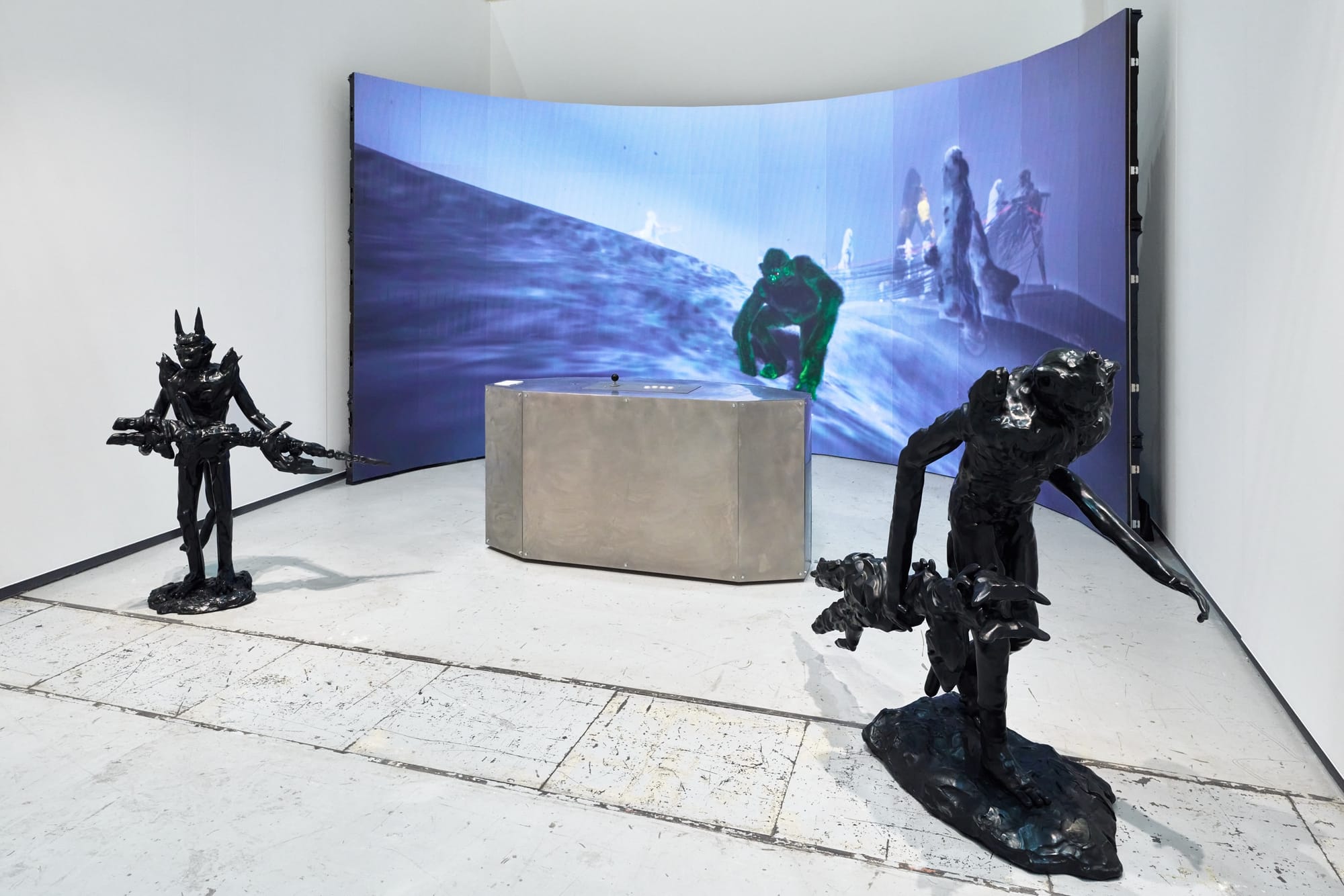 A curved screen shows figures crossing a blue landscape behind two black sculptures in ANIMA KINESIS