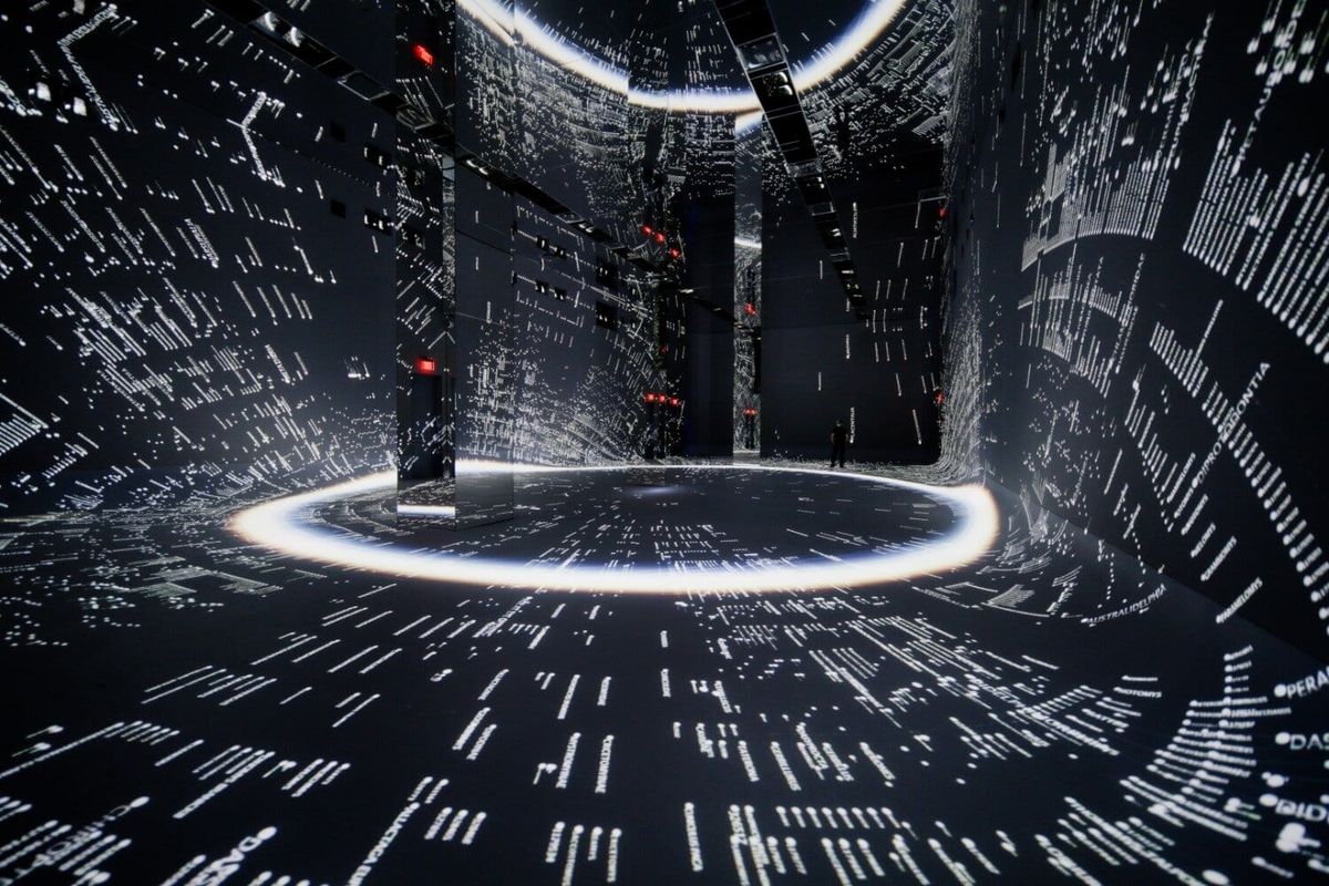 A large darkened gallery filled with floor-to-ceiling generative projections of foliage
