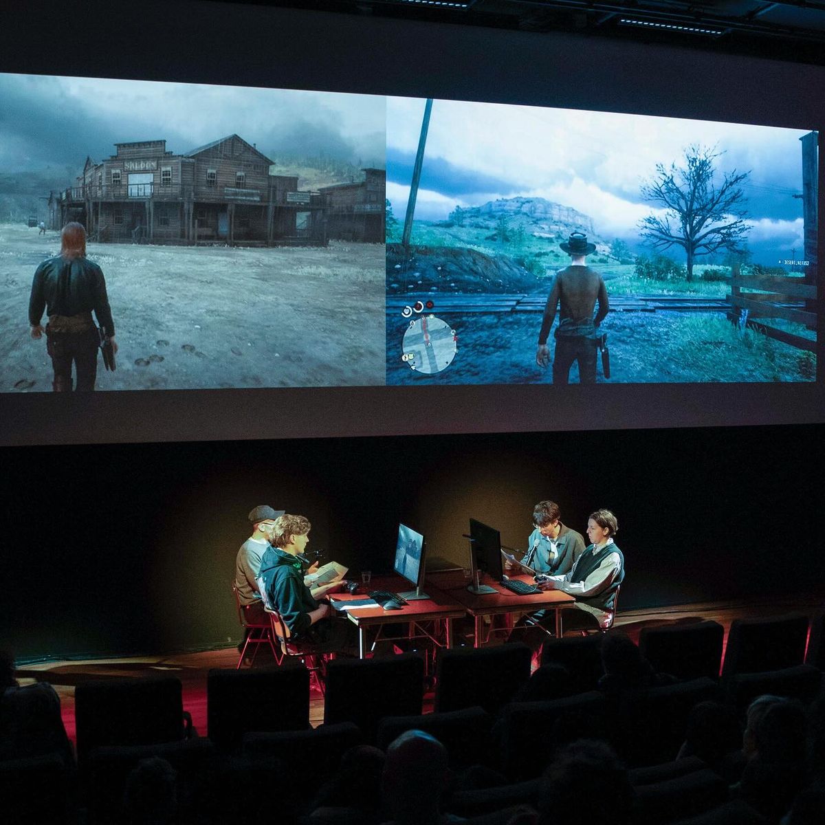 Performers seated at desks on a stage beneath two large projections of Red Dead Online, each showing a cowboy figure in a desert landscape