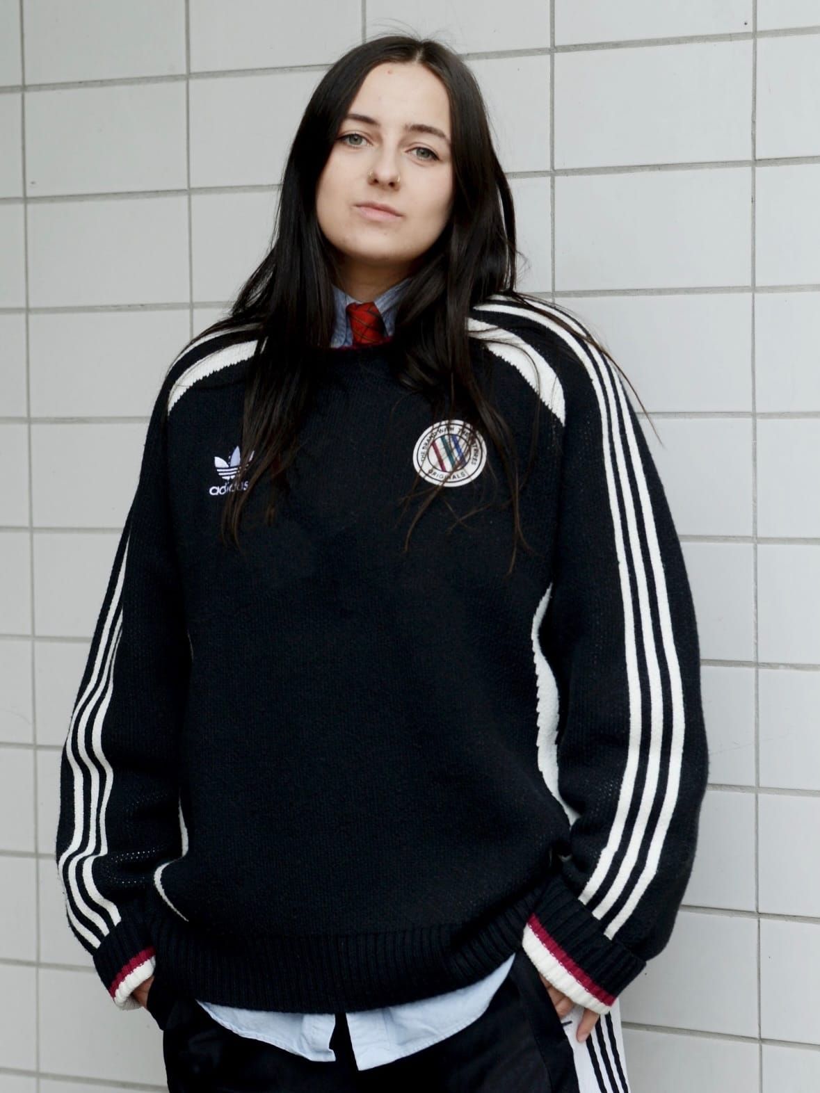 Lou Fauroux stands against a white tiled wall wearing a black track jacket.