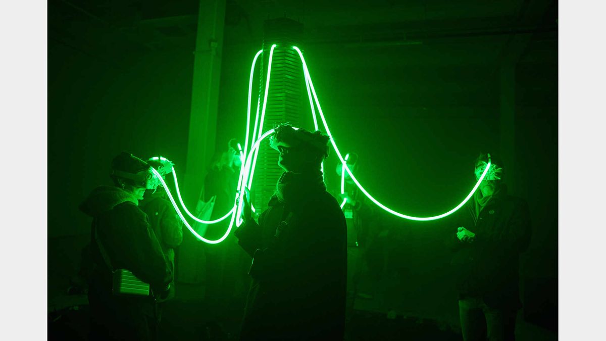 Masked participants stand in green light, connected by a glowing cable