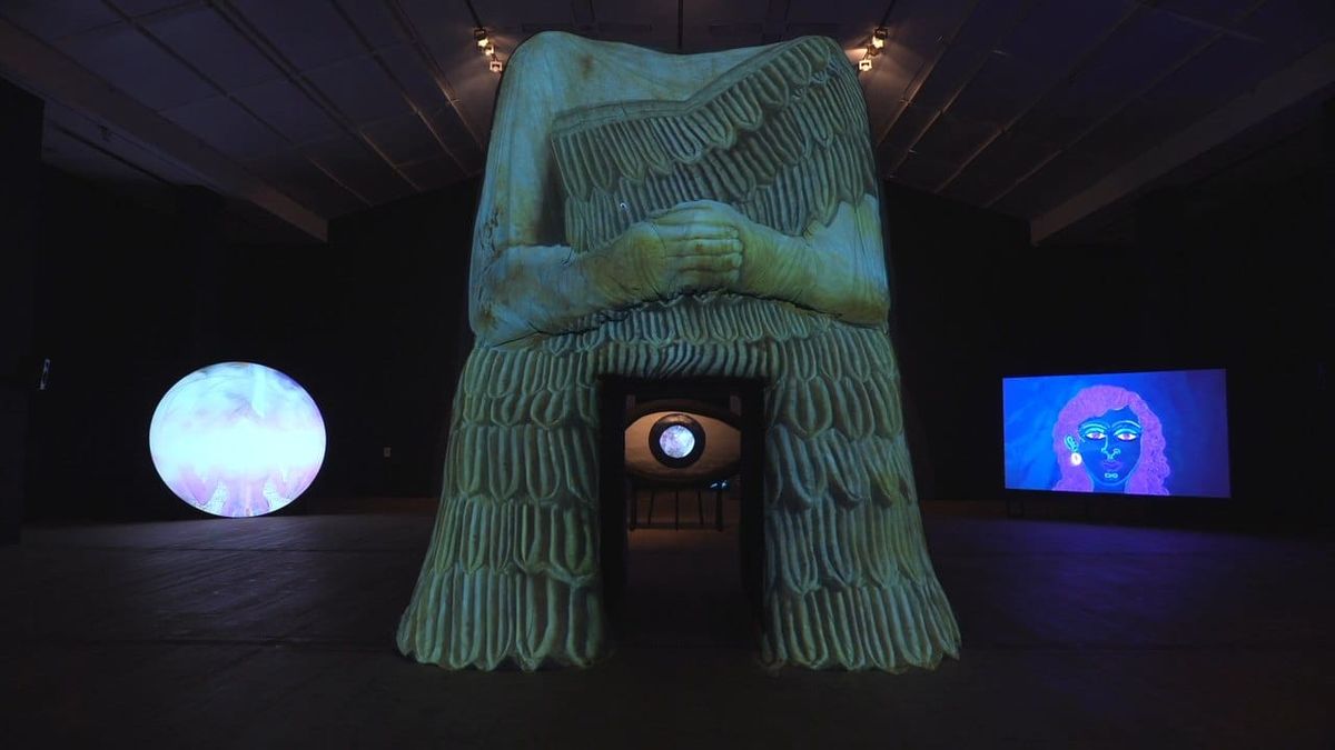 A monumental headless votive figure with a glowing projected eye in its doorway, at BALTIC