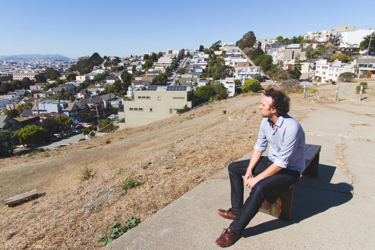 Marc ten Bosch sits on a wooden bench atop a dry hillside, looking out over San Francisco